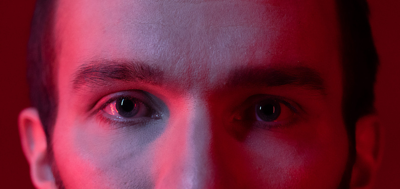Nuoren miehen silmät lähikuvassa, punaisessa yökerhovalossa.