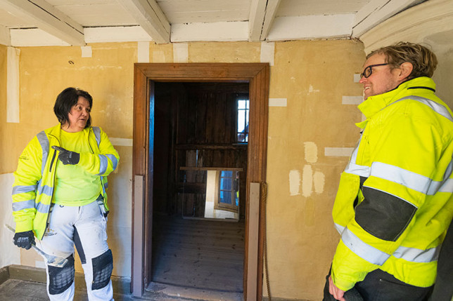 Lauri Leikas ja maalari Jaana Pamppunen seisovat vanhan puurakennuksen kamarissa. Keskustelevat keskenään. Tilan seinien paperipintojen maalaaminen on kesken.