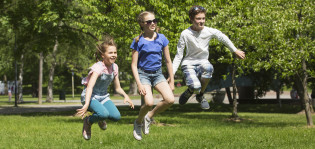 Kolme lasta hyppää ilmaan puistossa