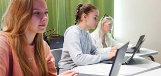 Kolme tyttöä tietokoneella oppitunnilla koulussa.