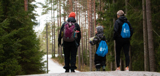 Perhe kävelee metsäpolulla reput selässä