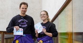 Kaksi opiskelijaa violeteissa haalareissa pitelevät Turun päivän appron karttaa Turun pääkirjaston edessä.
