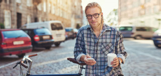 Mies nojaa kadulla polkupyöräänsä ja selaa puhelintaan kahvimuki kädessä