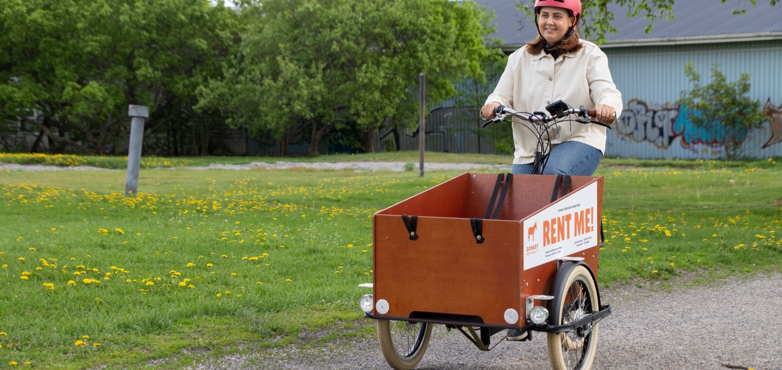 Nainen pyöräilee laatikkopyörällä alkukesän vehreyden keskellä