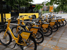 Fölläri kaupunkipyöriä rivissä pyöräpysäköinti paikassa, kaupunkibussin edessä.