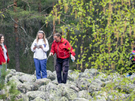 Pieni joukko ihmisiä seisoo kivien päällä metsämaisemassa