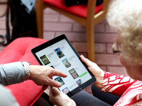Vanhempi nainen pitää tablet-laitetta ja toinen opastaa sen käytössä.