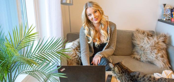 Helmi Lehtinen hymyilee kameralle kotisohvallaan läppärin ääressä. (Kuva: Lea Froloff)