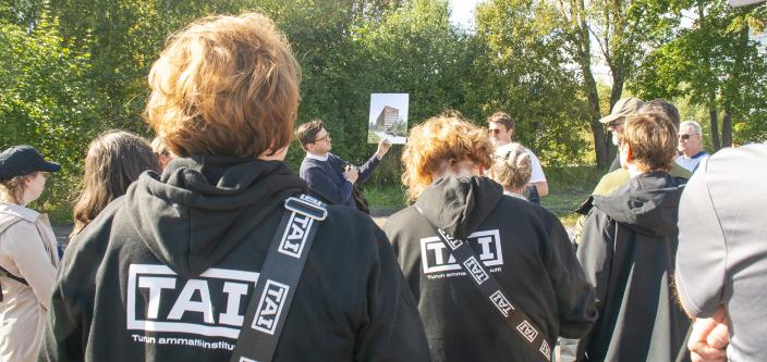 Eero Renell esittelee Taito-kampuksen havainnekuvaa etualalla näkyvälle yleisölle. (Kuva: Lea Froloff)