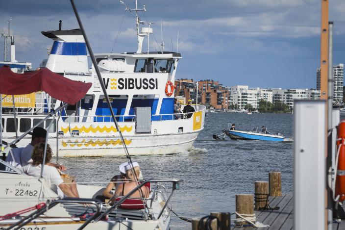 Valkokylkinen alus, jonka kyljessä lukee isolla "vesibussi", lähdössä aurinkoisena kesäpäivänä satamasta liikkeelle, ympärillä pienveneitä.  (Kuva: Pasi Leino)