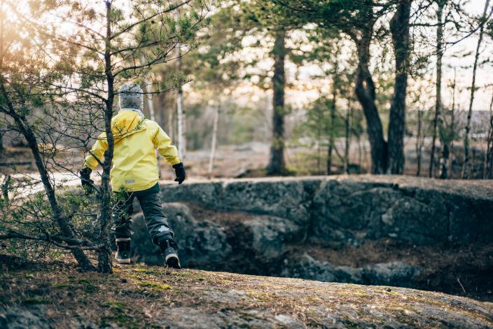 Lapsi keltaisessa asussa leikkii havumetsässä. (Kuva: Heikki Räisänen)