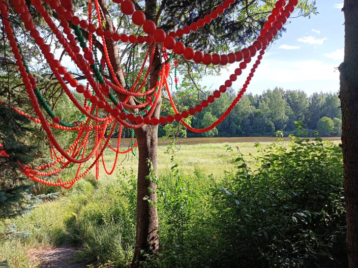 Puun oksalla roikkuvista punaisten pallojen ketjusta muodostuva taideteos. (Kuva: Sanna Majander)