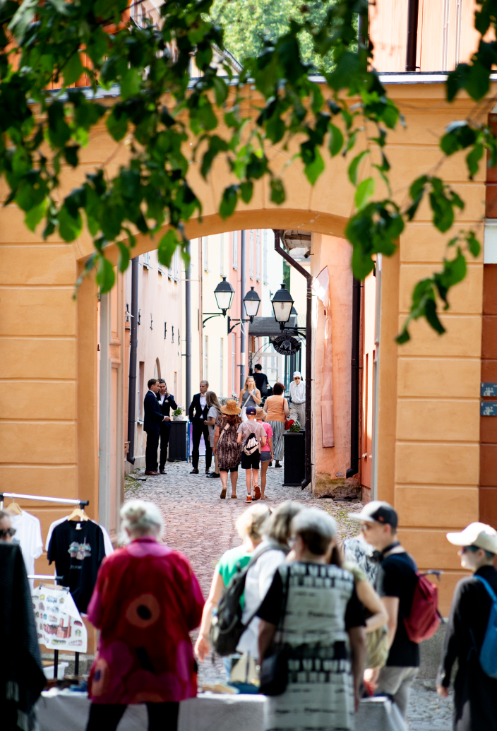 Kuvan edustalla on ihmisiä markkinapöydän luona. Takana näkyy muusikoita ja muuta väkeä Luostarin välikadulla. (Kuva: Anna-Rosa Eerikäinen)