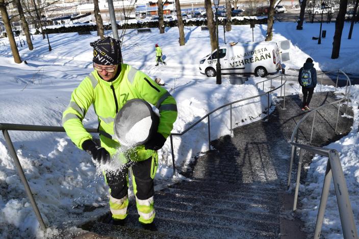 Työntekijä levittää kädellä ämpäristä suolaa puiston kulkuportaille. (Kuva: Annika Kujanpää)