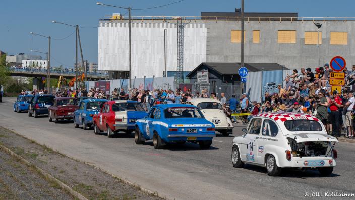 Klassikkoautot ajavat näytösluontoisesti Teollisuuskadulla yleisön seuratessa katsomosta. Kirkas sää houkuttelee paikalle runsaasti tapahtumavieraita. (Kuva: Itäharjun Ajot)