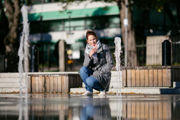 Nainen on kyykistynyt alas ja kuvaa Turun Kauppatorilla olevaa suihkulähdettä. (Picture: Åbo Creatives)