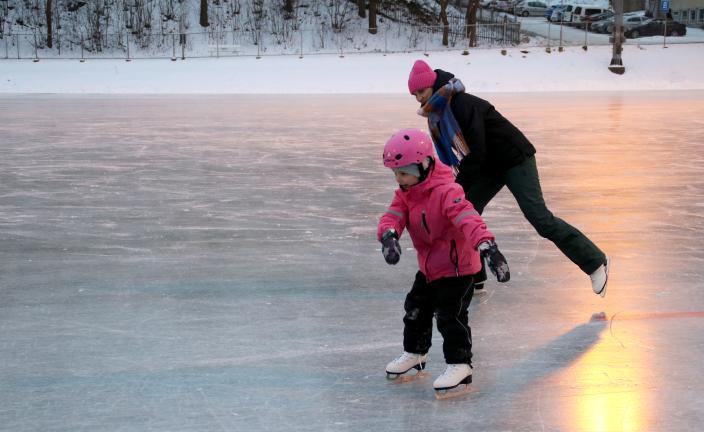 Lapsi luistelee luistelukentällä aikuisen kanssa. (Kuva: Kai Salonen)