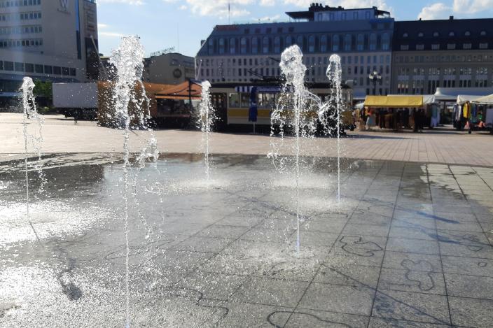 Turun Kauppatorin suihkulähteen vesipatsaat. Taustalla torikojuja ja Eerikinadun taloja. (Kuva: Susse Määttänen)