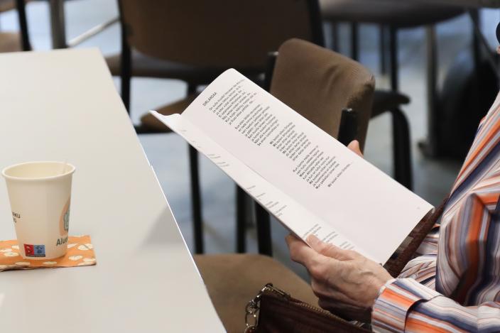 Henkilö lukee paperia pöydän ääressä. Pöydällä on kahvimuki, ja taustalla näkyy tuoleja. (Kuva: Oona Kokko)