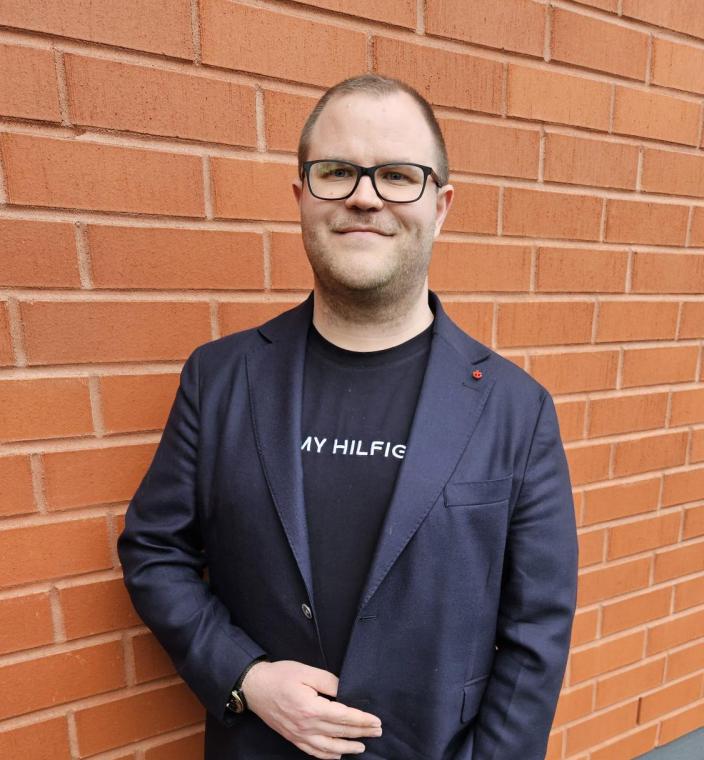 Antti Heikkilä seisoo punatiilisen seinän edessä.