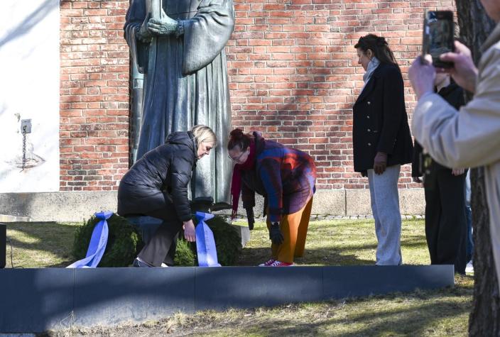 Kaksi naista laskee seppeleen patsaalle. 