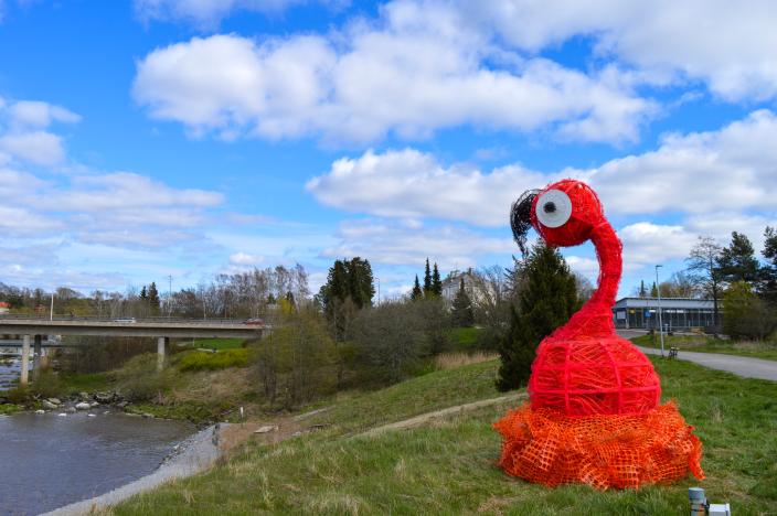 Vaaleanpunainen, flamingoa muistuttava veistos joen varressa. (Kuva: Ella Metsälä)