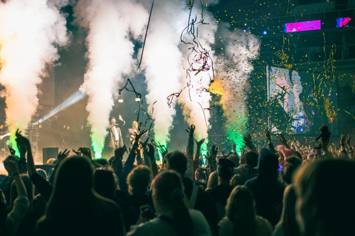 Kuvassa on iso joukko yleisöä selkä kuvaajaan päin. Yleisö katsoo suurta lavaa, josta suihkuaa savua ja konfetteja. (Kuva: Minttu Gummerus)