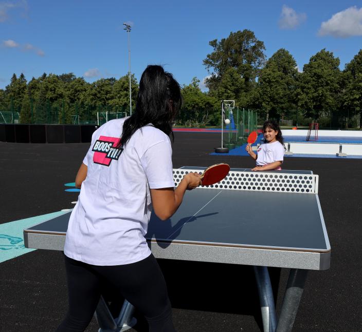 Nainen ja lapsi pelaavat pingistä aurinkoisena päivänä.