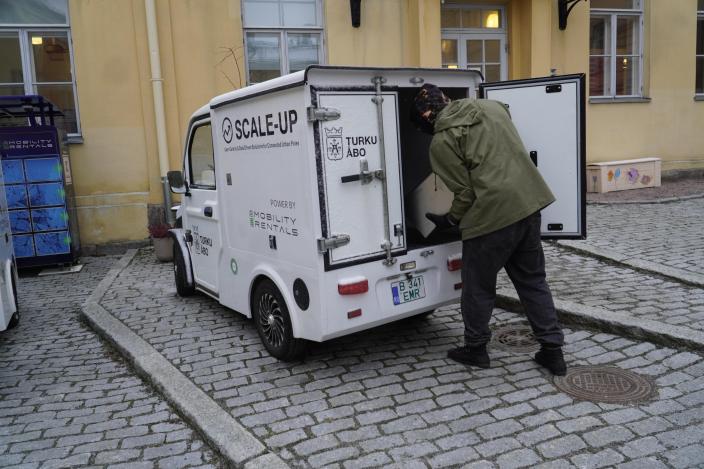 Mies seisoon minipakettiauton takana ja vaihtaa akkuja. (Kuva: Iiris Yli-Junnila)