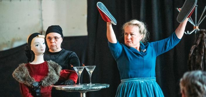 Kaksi henkilöä esiintyy Amiraalistonkadun vanhassa ratikkahallissa. Toisella heistä on sylissään nukke. Toinen on nostanut kätensä ylös ja pitelee käsissään kenkiä. (Kuva: Jussi Virkkumaa)