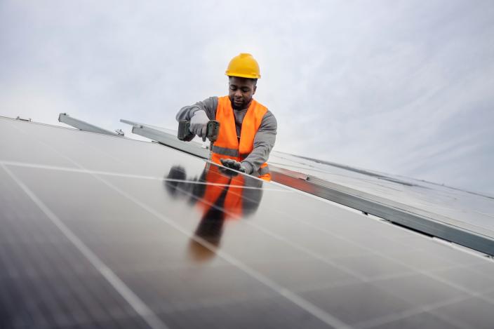 Työmies asentamassa aurinkopaneeleja talon katolle. Ilme on keskittynyt. (Kuva: Adobe Stock)