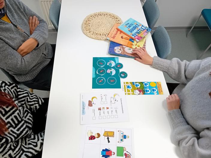 Pöydällä kirjoja ja esitteitä, sekä kolmen henkilön kädet. (Kuva: Jatta Kalasniemi)