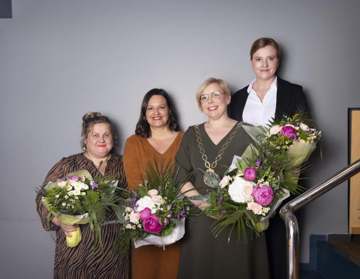 Neljä naista rivissä kukat kädessä.