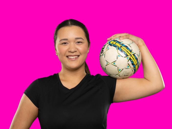 Nuori henkilö pitää jalkapalloa käsivarrellaan ja hymyilee iloisesti. (Kuva: Jussi Vierimaa)