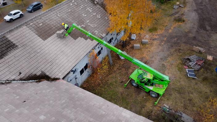 Henkilö purkaa teollisuusrakennuksen kattotiiliä nosturista käsin. (Kuva: Rabbit Visuals)