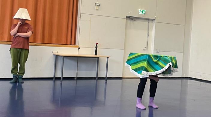 Kaksi esiintyjää sisätilassa: toisella lampunvarjostin peittää pään, toinen on värikkään kankaan alla. (Foto: Sandrina Lindgren)