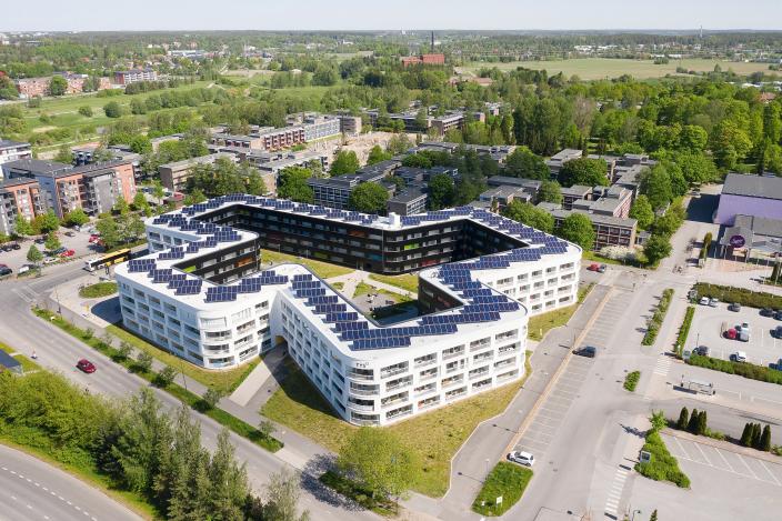 Ilmakuvassa aurinkopaneeleja modernin, valkoisen plus-merkin muotoisen kerrostalon katolla. (Kuva: Turun ylioppilaskyläsäätiö)