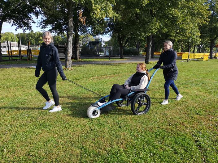 A woman sits in an all-terrain wheelchair being pulled and pushed across the lawn. (Picture: Johanna Friman)