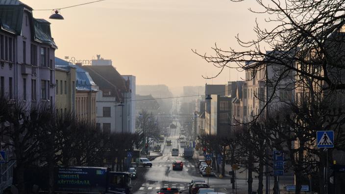 Kadulla keskustan kivitalojen keskellä autoja aamuhämärissä. Taivas on katupölystä harmaa. (Kuva: Hans-Peter Huhtala)