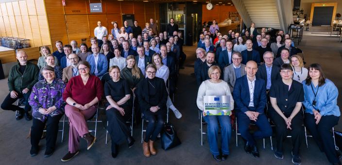 Pormestarin ilmastokokouksen osallistujat poseeraavat istualteen valokuvaajalle, keskellä pormestari Piia Elo. (Foto: Heikki Räisänen)