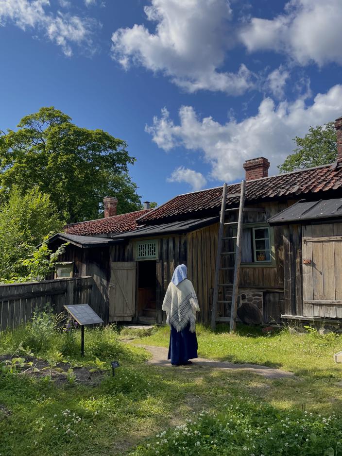 1800-luvun vaatteisiin pukeutunut nainen seisoo Luostarinmäen sisäpihalla. (Kuva: Mireka Haapanala)