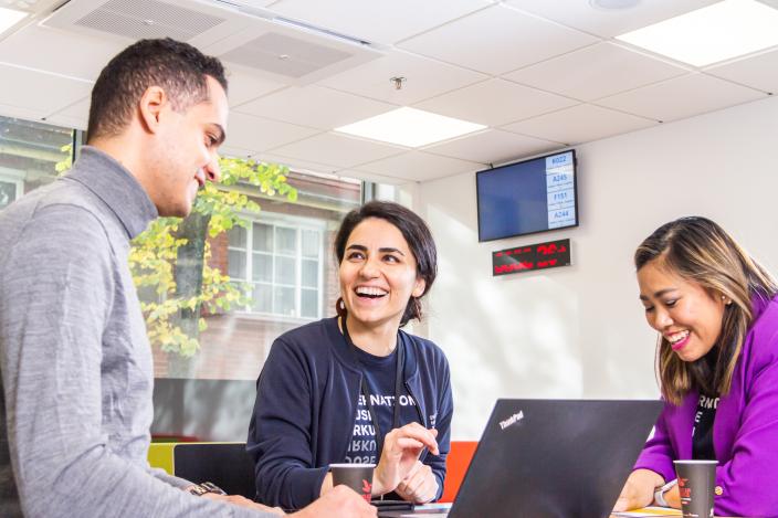 Kuvassa kolme nauravaa ihmistä, keskimmäisellä päällään International House Turku -paita.