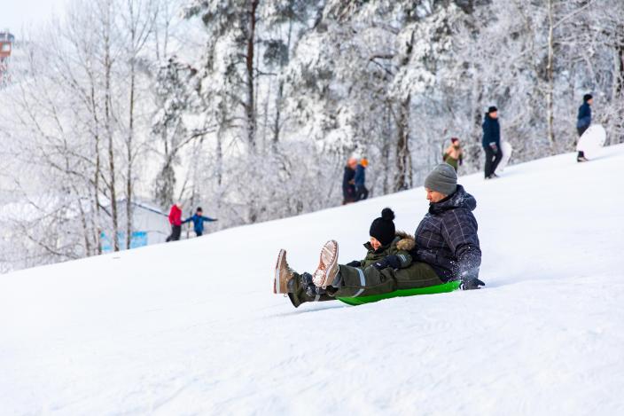 Vanhempi ja lapsi laskevat pulkalla lumista mäkeä alas. (Kuva: Heikki Räisänen)