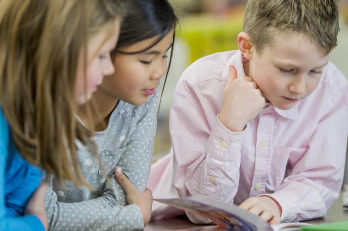 Kolme oppilasta lukee kirjaa luokkahuoneessa. (Kuva: iStock_kuvapankkikuva)