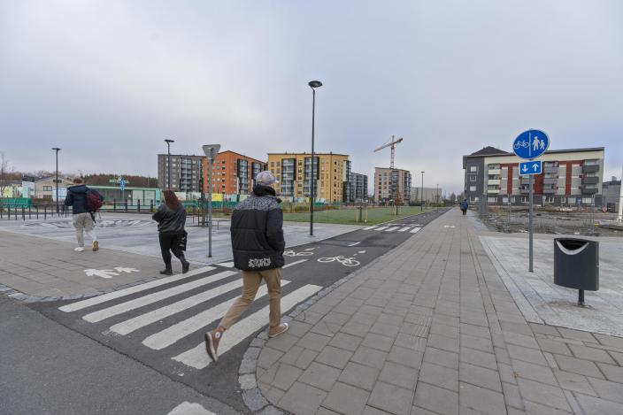 Etualalla risteävät uudella asuinalueella olevat kävely- ja pyöräilytiet. Kävelyteillä on jalankulkijoita. Taustalla vasemmalla näkyy viheralue ja sen jälkeen kauempana erivärisiä kerrostaloja ja rakennusnosturi. (Kuva: Timo Jakonen)