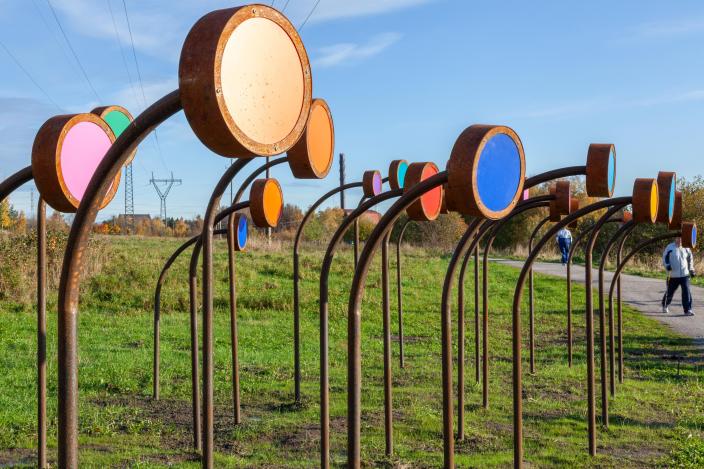 Ruosteenruskeat teokset, joissa värikkäät valokalvot, taipuvat kuten ketojen kukat kohti ohikulkevaa ulkoilijaa.