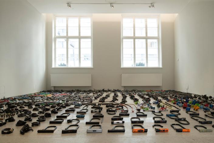 Kuvassa museotilassa pyörälukkoja ja muita pyörätarvikkeita pitkin lattiaa.