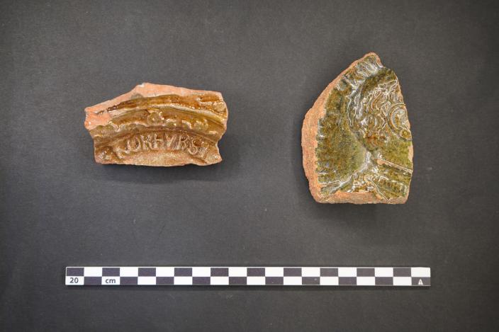 Kaksi vihreänruskeaa, lasitettua kaakelinpalasta. Toisesta erottuu selvästi juhla-asuun pukeutuneen miehen takaraivo profiilissa. (Kuva: Johanna Joensuu, Muuritutkimus Oy)