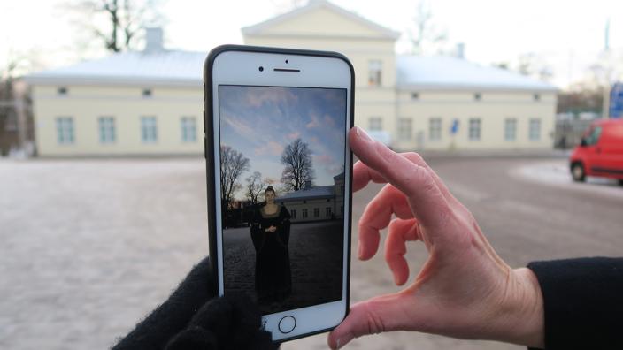 Kädessä oleva puhelin, jonka ruudulla näkyy naishahmona Kaarina Maununtytär. (Foto: Teija Murmann)