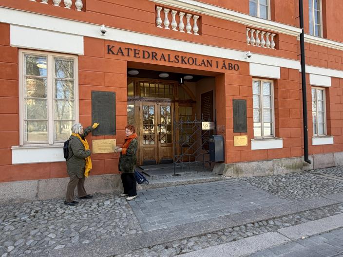 Kaksi naista tutkii muistolaattaa Katedralskolanin pääoven edessä. (Kuva: Hannele Sivonen)